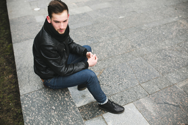 A man dressed in jeans and black jacket seats on a slab - Fotoğraf, Görsel