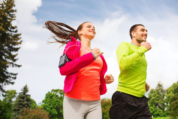 smiling couple with earphones running outdoors - Foto, immagini