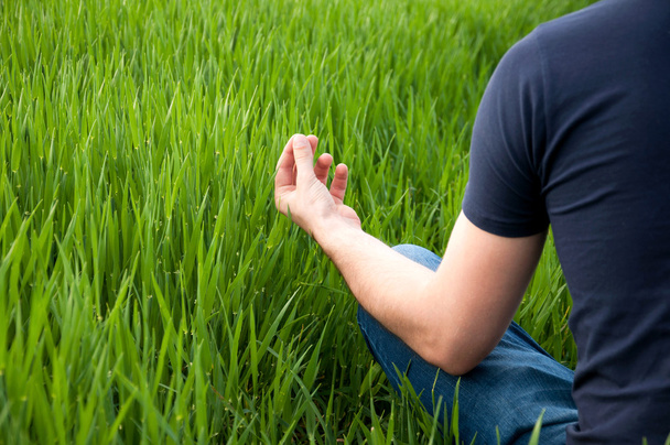 El hombre se sienta en medio de un prado verde
 - Foto, Imagen