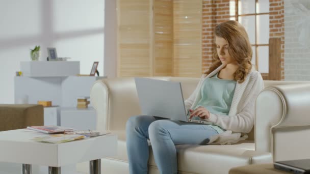 Beautiful young woman working on laptop in modern apartment - Кадри, відео