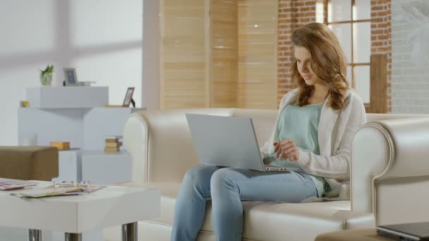 Happy young lady sitting at home, chatting on laptop, smiling - Materiał filmowy, wideo