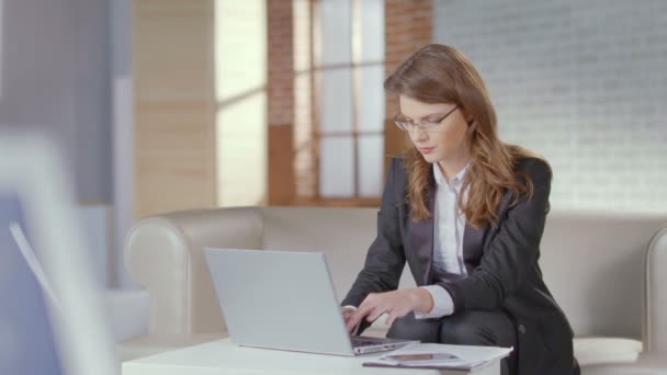 Lady in business suit, glasses works on laptop, smiles at camera - Imágenes, Vídeo
