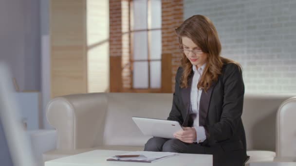 Pretty businesswoman works on tablet in office, smiles at camera - Filmmaterial, Video