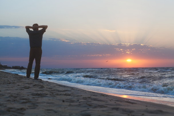 Человек смотрит на восход солнца на пляже
 - Фото, изображение