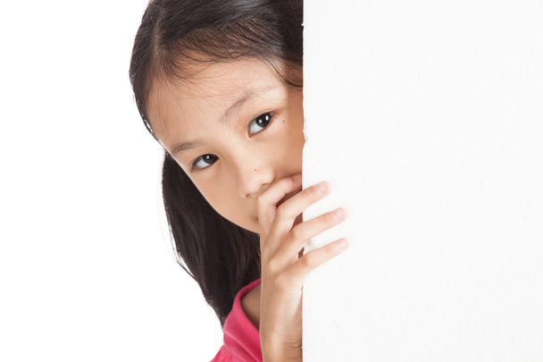 μικρό ασιατικό κορίτσι, κρυφοκοιτάζουν πίσω από έναν λευκό πίνακα - Φωτογραφία, εικόνα