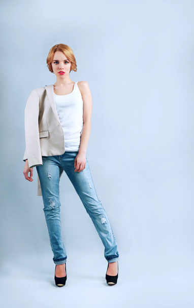Beautiful young woman in jacket and jeans posing on light background - Fotó, kép