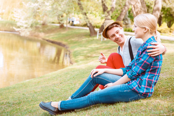 湖の近くの草の上に座っている若いカップル - 写真・画像