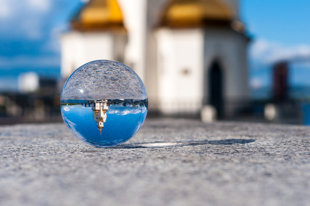 Bola transparente de vidrio sobre fondo de iglesia y superficie granulada. Con espacio vacío
 - Foto, Imagen