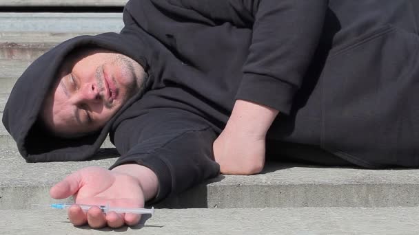 Huumeriippuvainen mies nukkuu ruisku kädessä ulkona
 - Materiaali, video