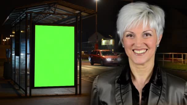Geschäftsfrau mittleren Alters lächelt - Bushaltestelle - Werbetafel - grüner Bildschirm - Nacht - Stadtstraße mit Autos - Filmmaterial, Video