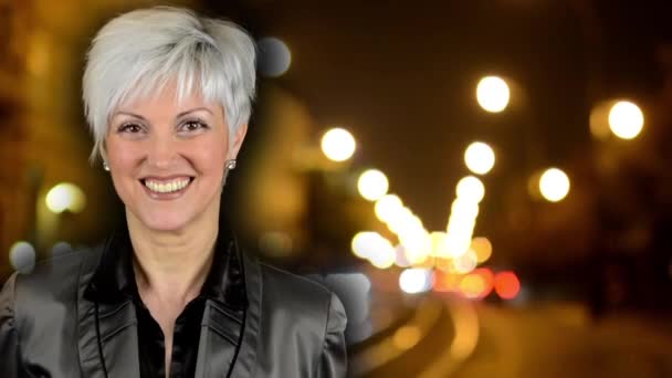 Geschäftsfrau mittleren Alters lächelt - Nacht Stadt - Nacht Straße mit Autos - Lampen-Auto Scheinwerfer - Gebäude - Zeitraffer - Filmmaterial, Video