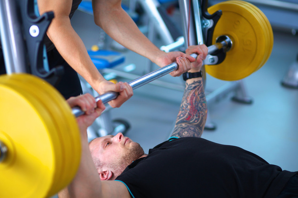 Young man lifting the barbell in gym with instructor - Foto, Bild