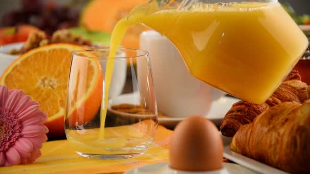 Llenado de vidrio con zumo de naranja en la mesa con desayuno
 - Metraje, vídeo