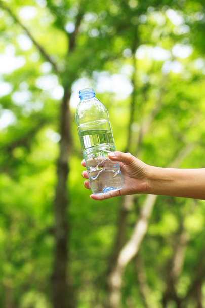 Stock Photo - Woman hand holding water bottle against green back - Foto, Bild