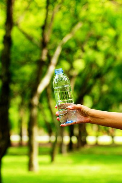 Foto stock - Mulher mão segurando garrafa de água contra as costas verdes
 - Foto, Imagem