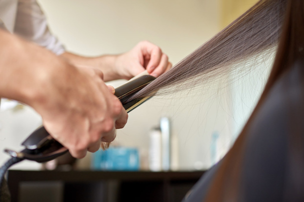 stylist with iron straightening hair at salon - Foto, Imagem