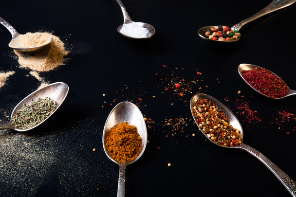 Spices in old metal spoons on black background - 写真・画像