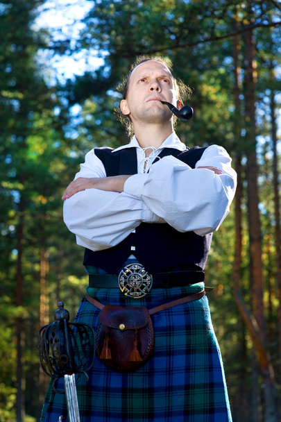 Человек в шотландском костюме с мечом и трубкой
 - Фото, изображение