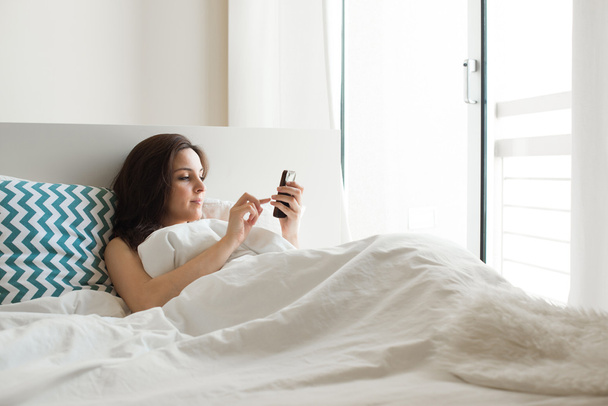 Yatakta akıllı telefonlu bir kadın - Fotoğraf, Görsel