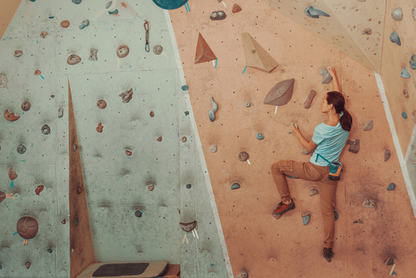 Young woman climbing artificial boulder in gym - Фото, изображение
