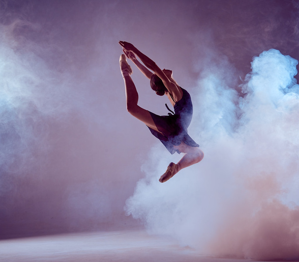 Beautiful young ballet dancer jumping on a lilac background.  - 写真・画像