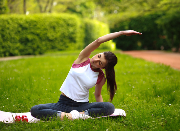 Sportive mladá žena, strečink, dělá fitness cvičení v parku - Fotografie, Obrázek