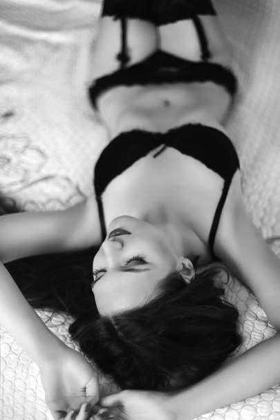 Tempting slim girl in black lingerie lying on bed. Brunette woma - Photo, Image