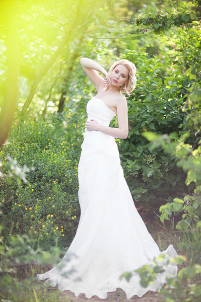 beautiful elegant bride with blond hair posing in the green forest - 写真・画像
