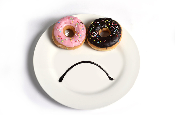 droevig smileygezicht maakte op schotel met donuts als ogen en chocolade siroop mond in suiker zoete verslaving dieet en voeding - Foto, afbeelding
