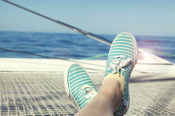 woman relaxing on a catamaran sailboat trampoline with her feet crossed - Fotó, kép