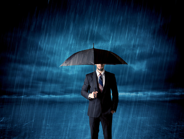 Business man standing in rain with an umbrella - 写真・画像