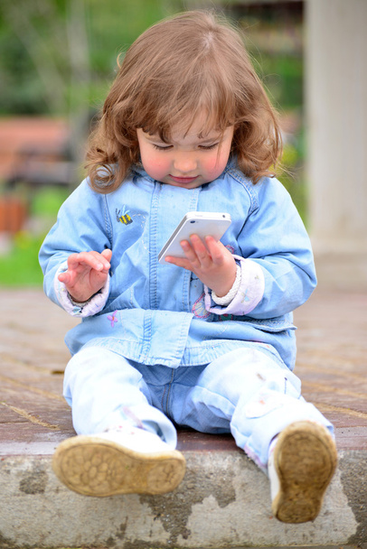 Girl two years, with a cell phone in the park - Photo, Image