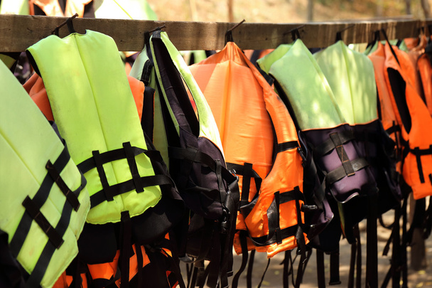 Разноцветные спасательные жилеты висят в ряд
 - Фото, изображение