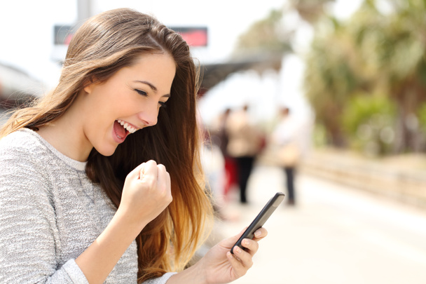 Mutlu kadın akıllı telefonunu bir tren istasyonunda izlerken - Fotoğraf, Görsel