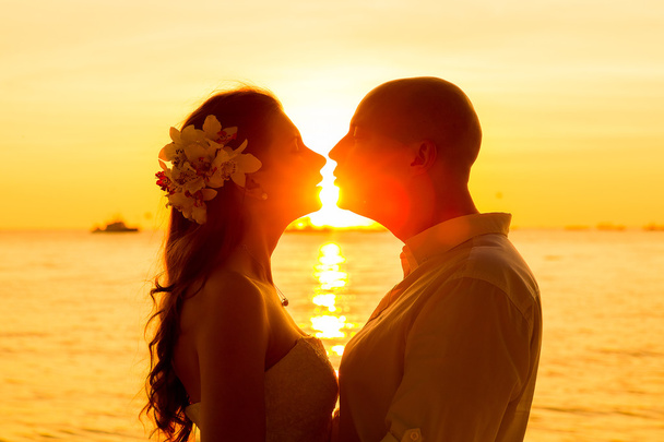 νύφη και γαμπρός φιλάει σε μια τροπική παραλία στο ηλιοβασίλεμα - Φωτογραφία, εικόνα