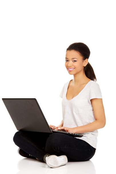 Teen sitting cross legged with laptop. - Zdjęcie, obraz