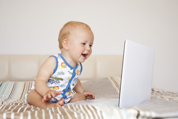 Baby with computer sitting on the bed - Photo, Image