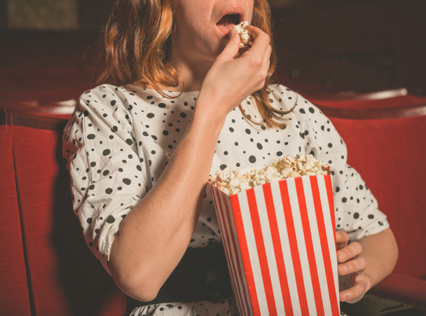 Νεαρή γυναίκα τρώγοντας ποπ κορν στο σινεμά - Φωτογραφία, εικόνα