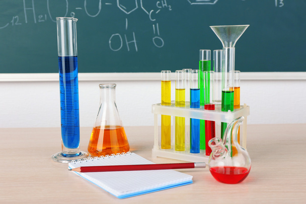 Desk in chemistry class with test tubes on green blackboard background - Foto, imagen