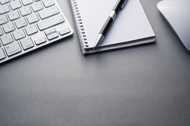 Tastatur, Maus und Notizbuch mit Stift auf grauem Schreibtisch - Foto, Bild