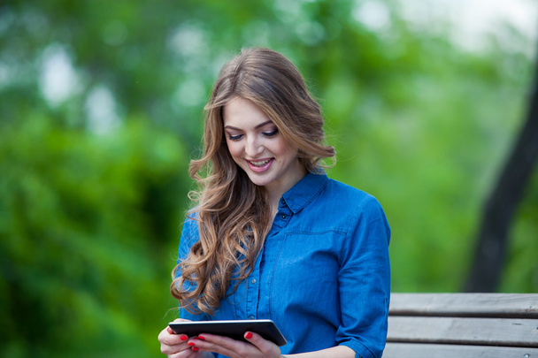Side view of a young woman using  tablet computer on  park bench - 写真・画像