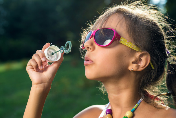 Cute little girl is blowing a soap bubbles on the green grass - Fotoğraf, Görsel