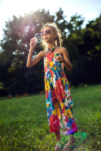 Cute little girl is blowing a soap bubbles on the green grass - Fotografie, Obrázek
