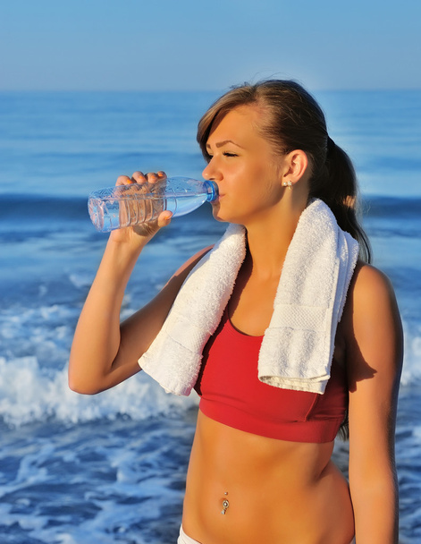 Menina bonita beber água após o exercício na praia
 - Foto, Imagem