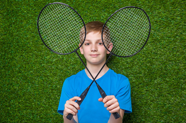 Happy boy holding badminton rackets over grass - Foto, Imagem
