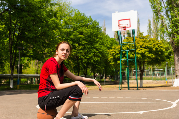 Athletic Woman Sitting on Basketball on Court - Photo, image