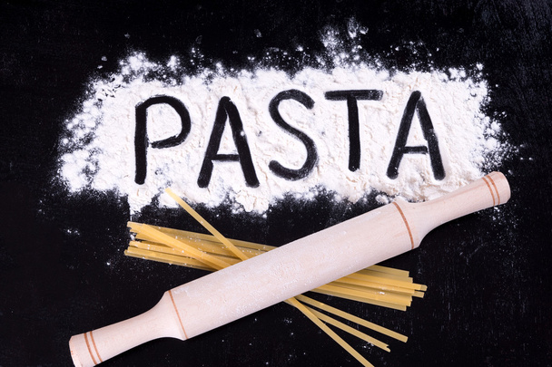 On written flour pasta. Dark background. Rolling pin lies on macaroni. Top view. - Фото, зображення