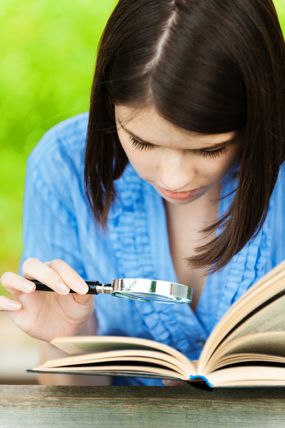 Portrait young woman reading book magnifier - Photo, Image