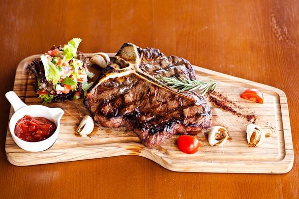 Club hovězí steak s paprikovou omáčkou a grilovanou zeleninou na řezací desce na tmavém dřevěném pozadí - Fotografie, Obrázek
