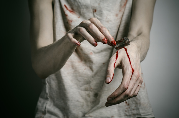 Depression and bloody Halloween theme: a man holding a bloody razor for suicide on a gray background in the studio - Фото, изображение